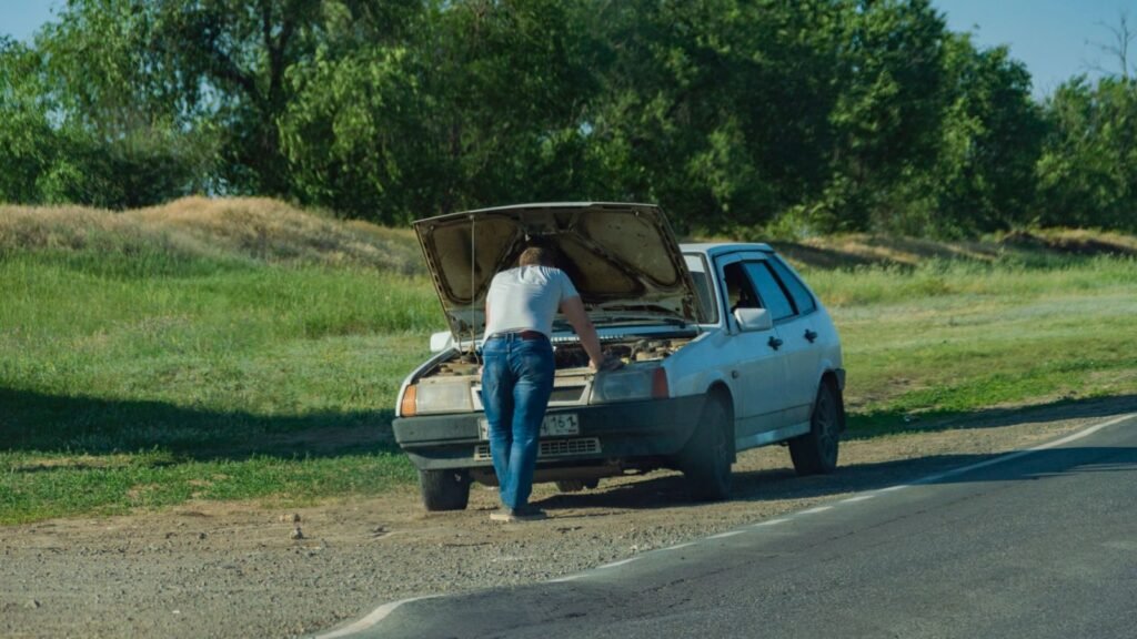 Motorista com o cofre aberto de um carro parado na estrada: carro morre em marcha lenta